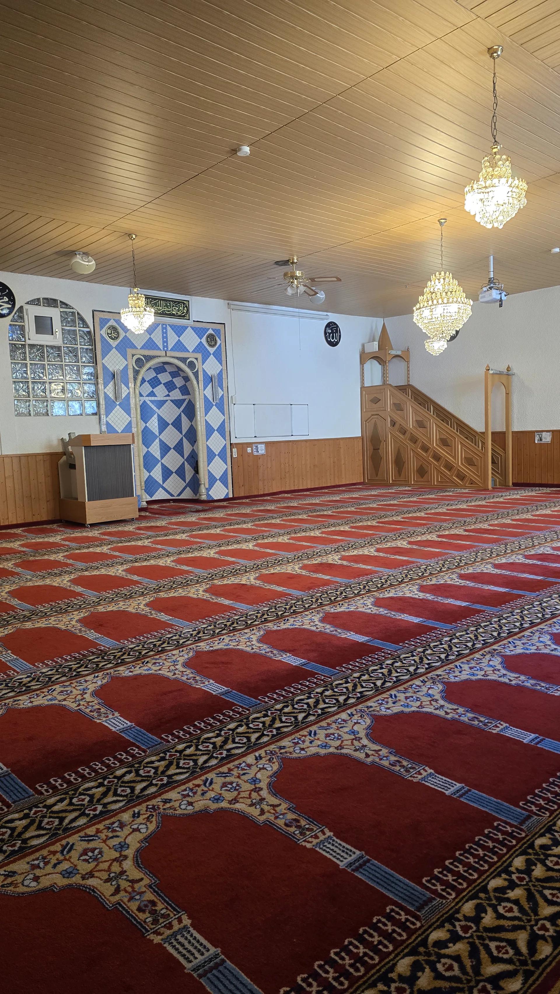 Leerer Gebetsraum mit Mihrab, Minbar und ausgerichteten Teppichreihen