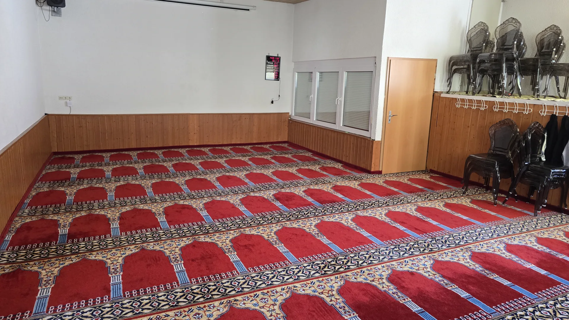 Ein Nebenraum der Moschee mit Gebetsteppich, Garderobenhaken an der Wand und gestapelten Stühlen