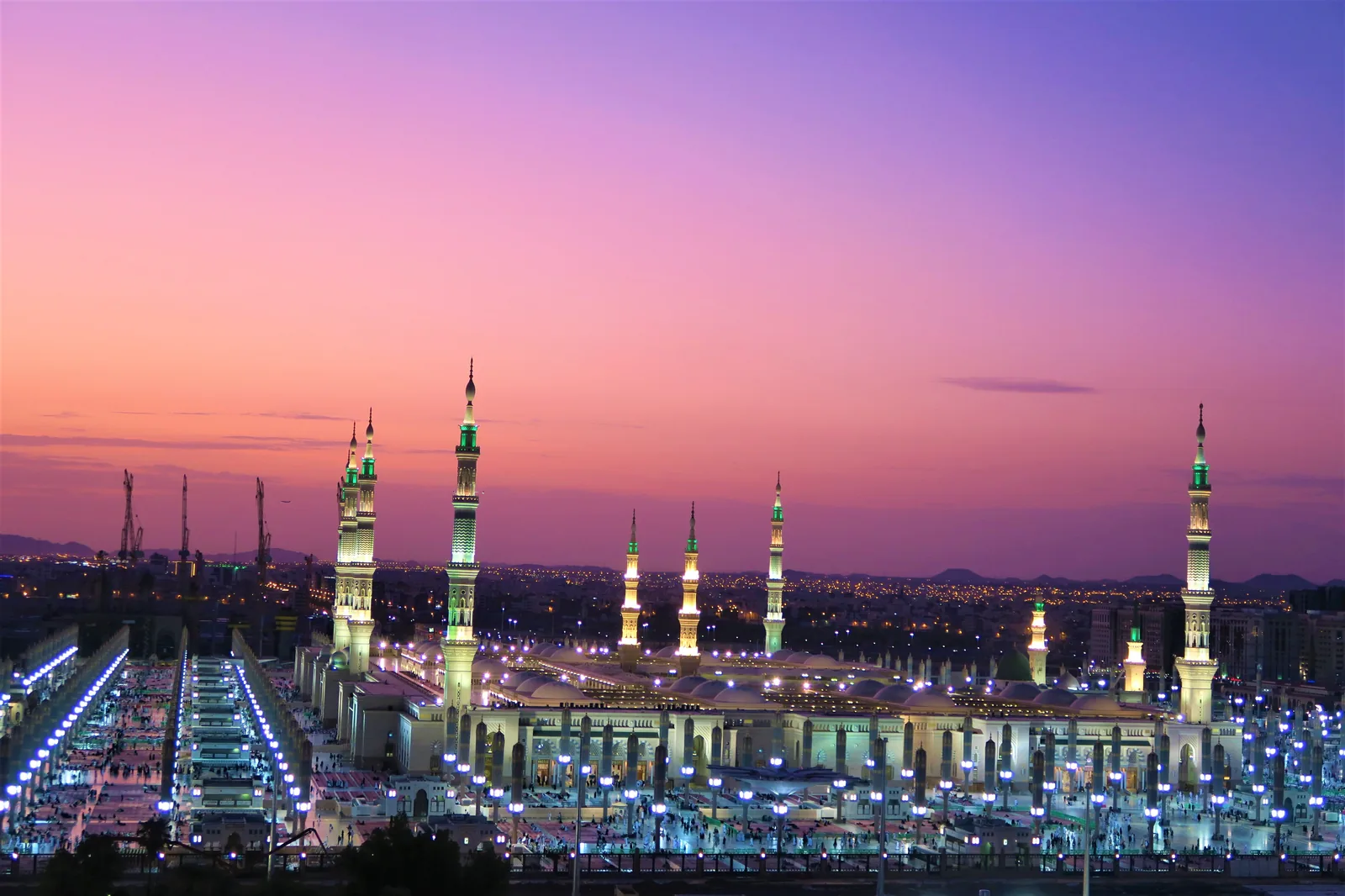 Die Prophetenmoschee in Medina in der Abenddämmerung, die beleuchteten Minarette vor violettem Himmel.